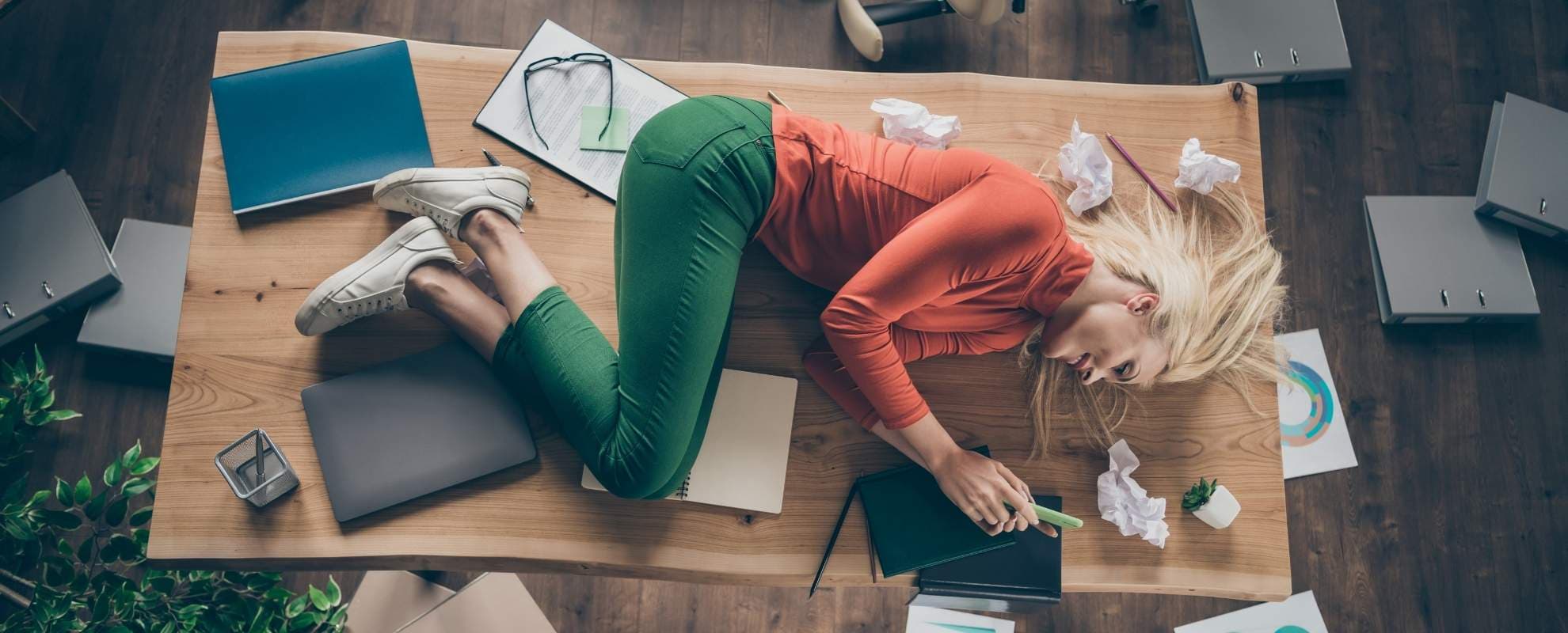 Exhausted woman lying on a desk among scattered papers and folders
