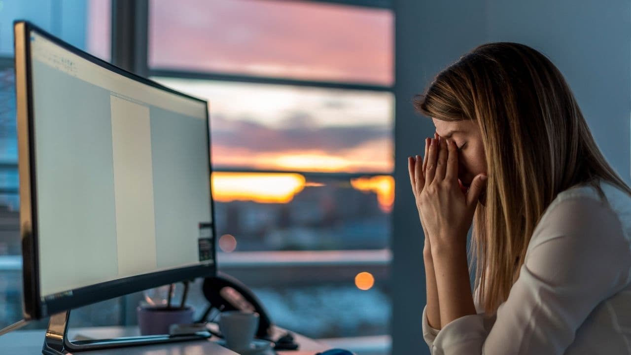 Businesswoman sitting in front of the computer with her hands on her head, looking stressed and blocked: innovation jam, no creative ideas possible. Caused by chaos and high entropy, a creative block in the work environment.