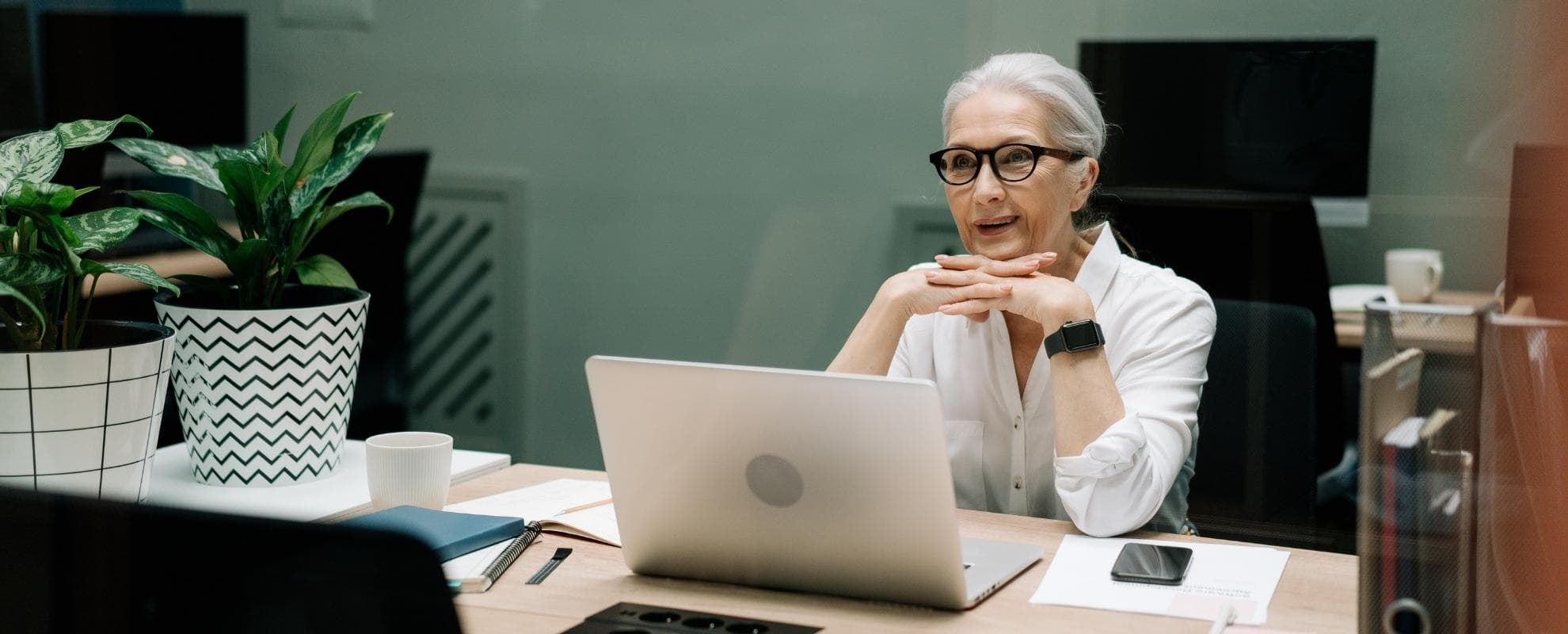 Older woman with grey hair and glasses sitting attentively at a laptop