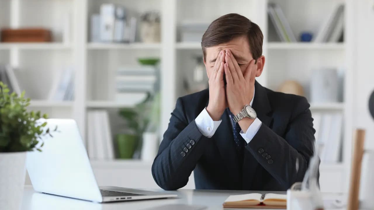 Überforderter Geschäftsmann sitzt am Laptop und hält sich die Hände vors Gesicht