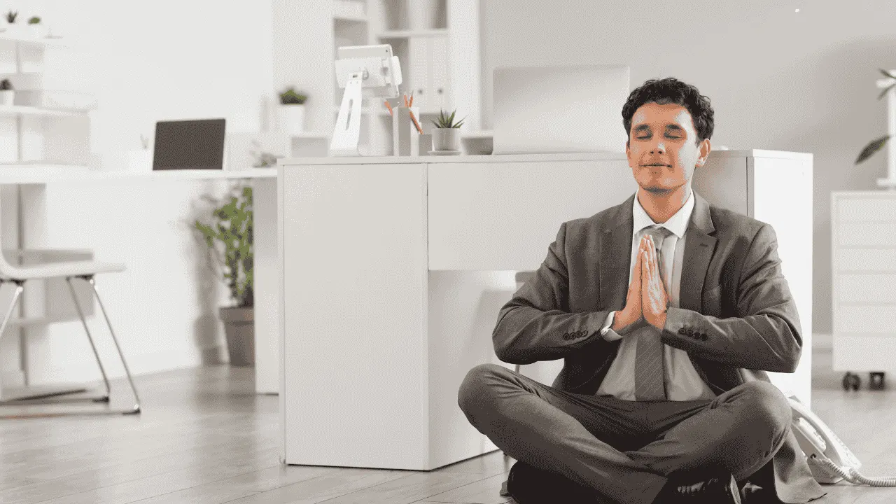 Businessman meditating cross-legged on the floor of a bright office