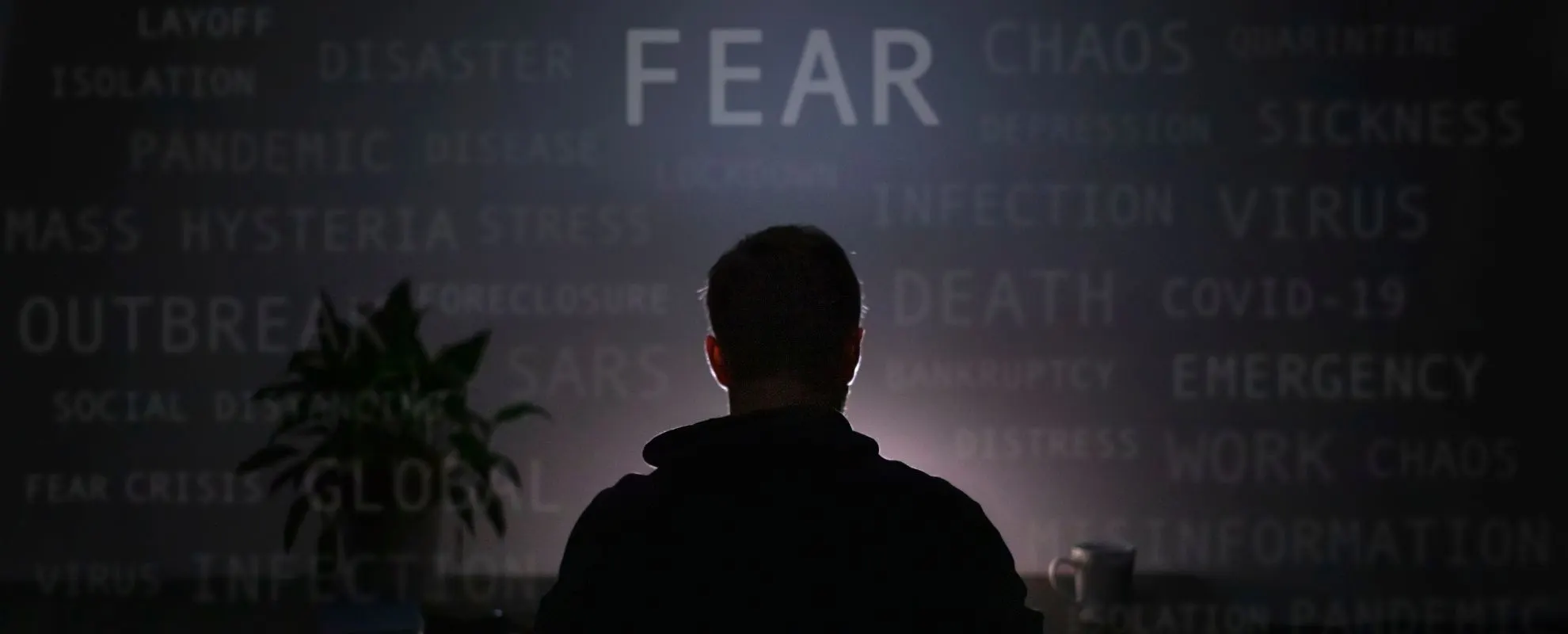 Silhouette eines Mannes vor einer Wand mit Wörtern wie Fear, Chaos, Crisis und Panic