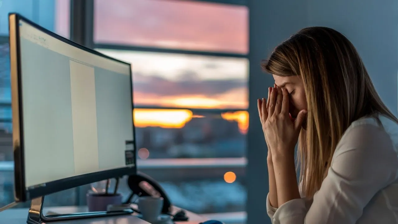 Businesswoman sitting in front of the computer with her hands on her head, looking stressed and blocked: innovation jam, no creative ideas possible. Caused by chaos and high entropy, a creative block in the work environment.