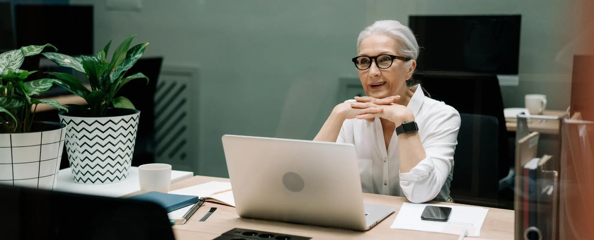 Ältere Frau mit grauen Haaren und Brille sitzt aufmerksam am Laptop