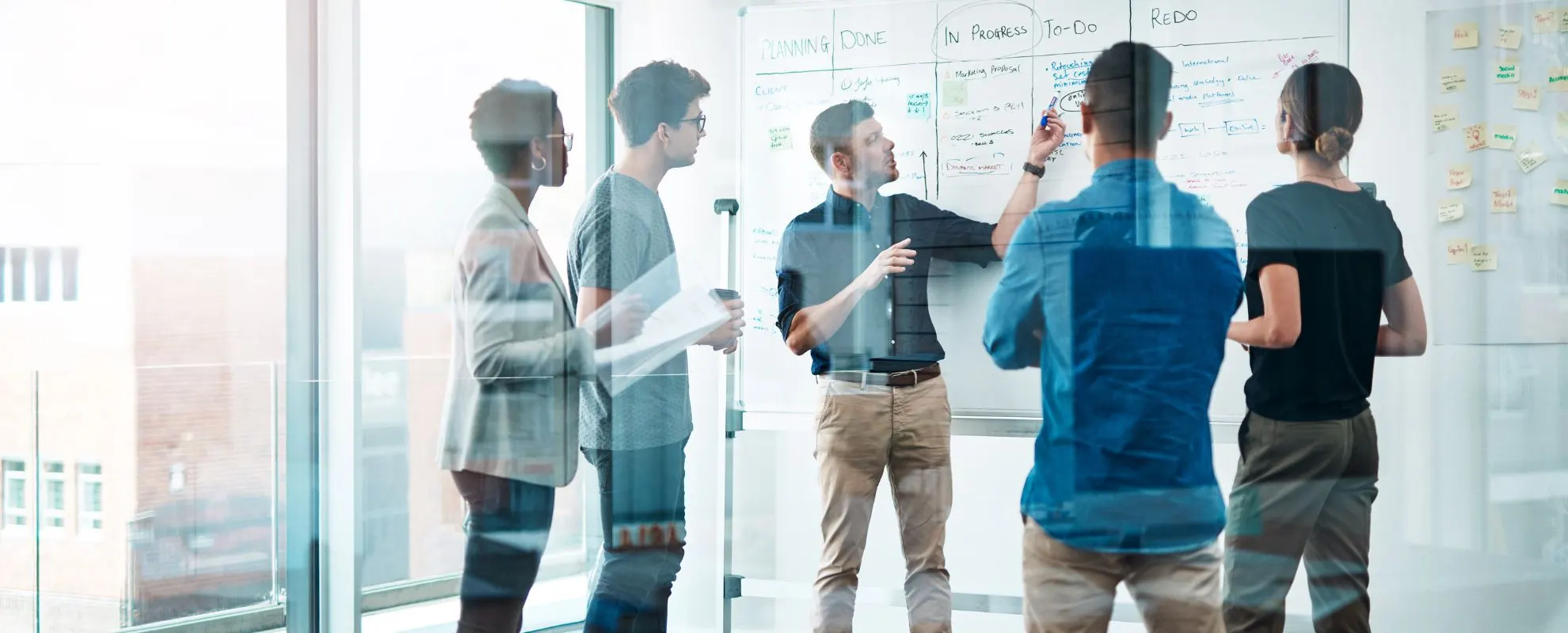 Team standing in front of a glass wall with notes, discussing a plan