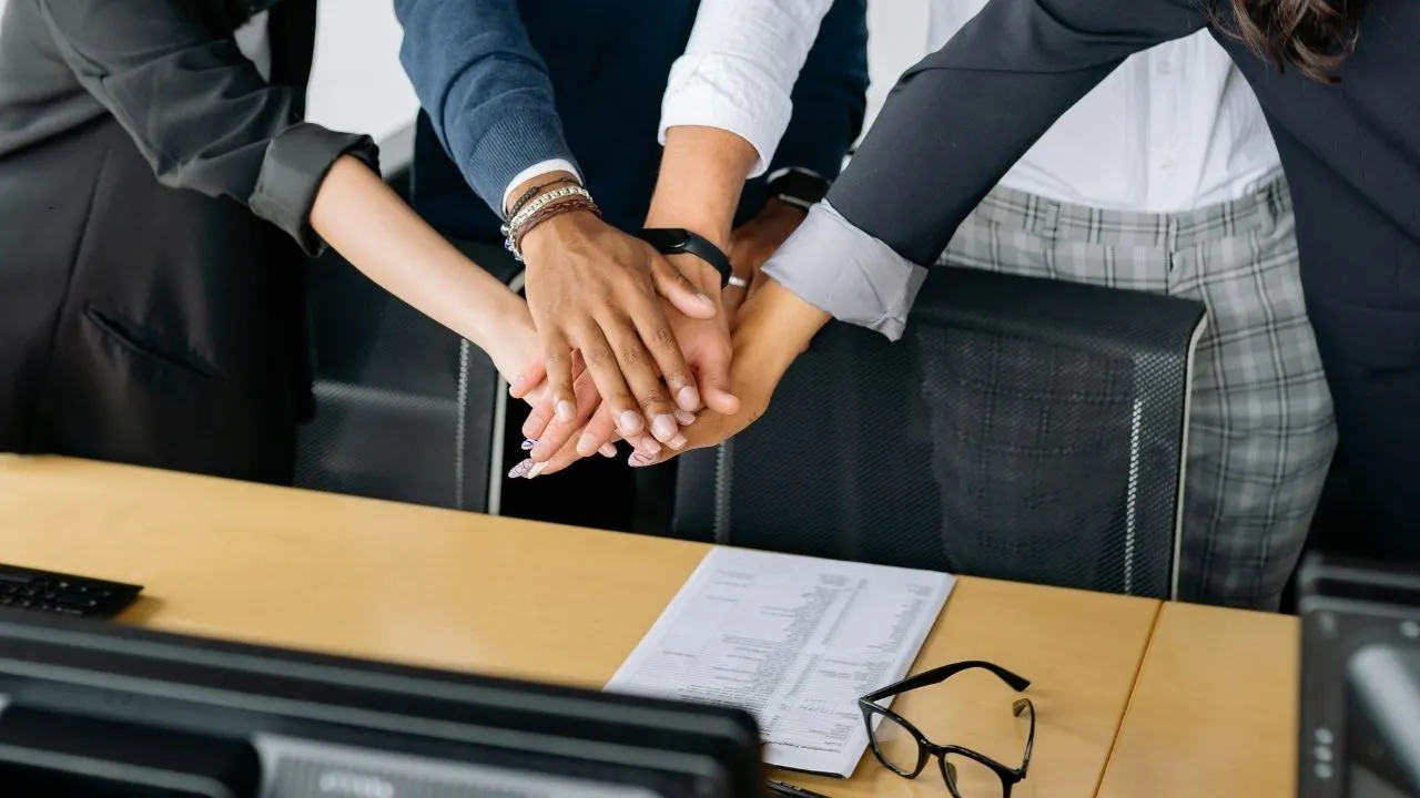 A team joins hands to symbolize cooperation, cohesion.