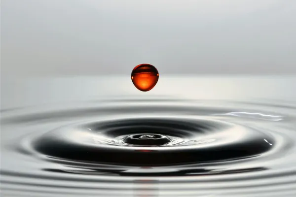 Ein Tropfen fällt auf eine Wasserfläche und zieht Kreise