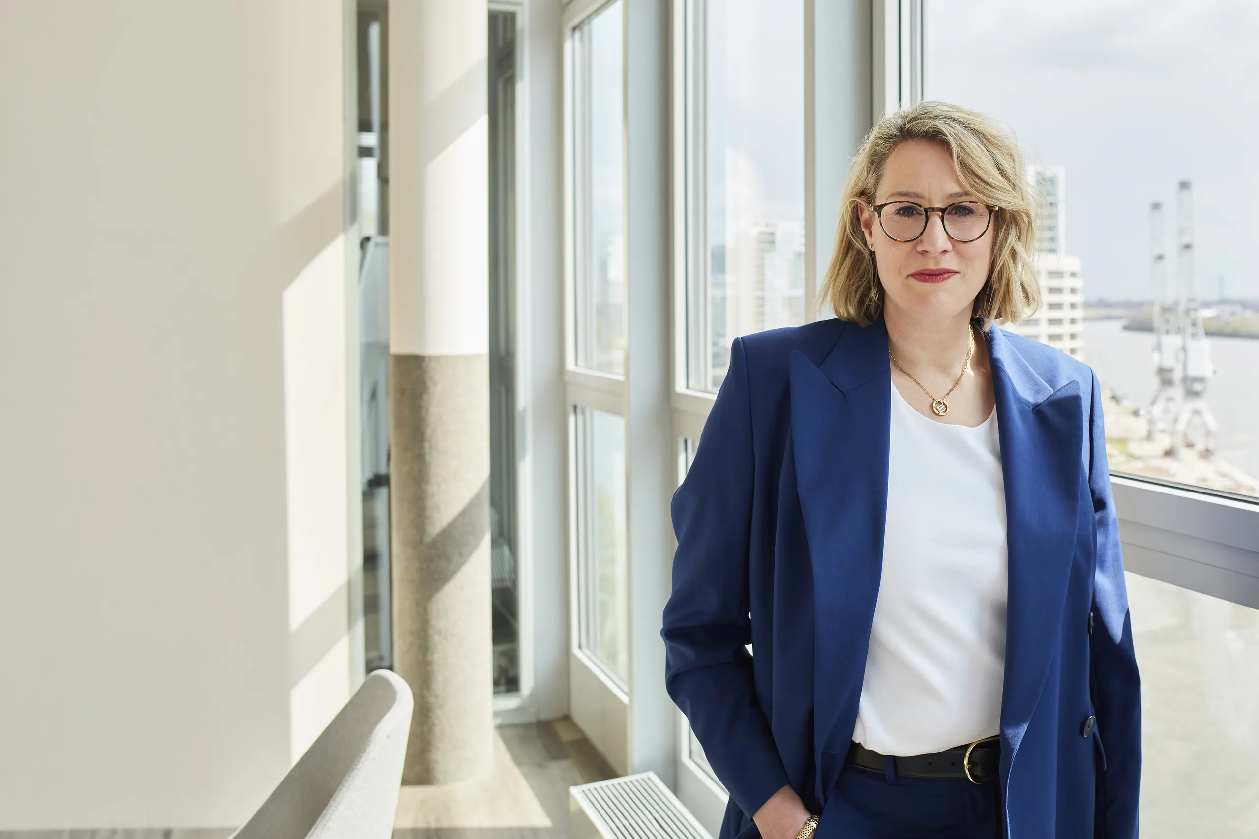Julie Sternberg im blauen Blazer am Fenster, im Hintergrund Hafenkräne